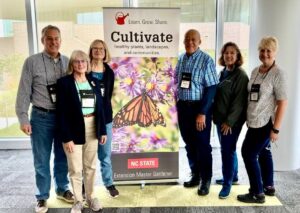 A group of Master Gardener volunteers pose for a picture beside a colorful banner.